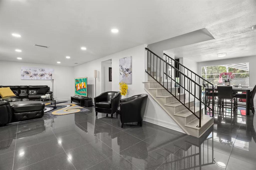 A living room with gray tile floors, a black leather sofa, and a staircase — 7005 FOUNTAIN AVENUE, TAMPA, FL