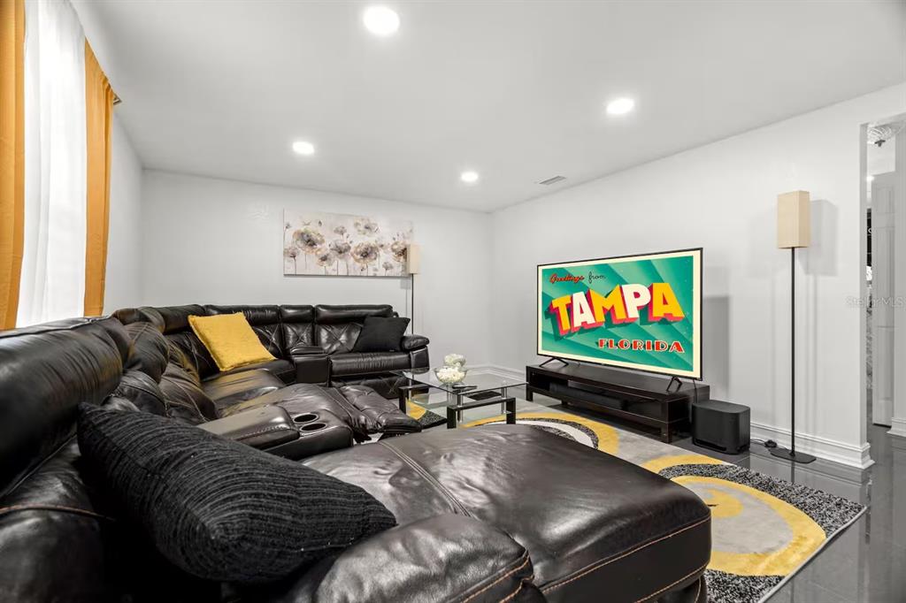 A living room features a large black leather sectional, a television, and a patterned rug — 7005 FOUNTAIN AVENUE, TAMPA, FL