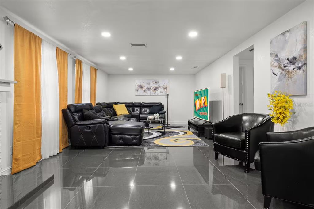 A living room features dark tile floors, a black sectional sofa, and yellow curtains — 7005 FOUNTAIN AVENUE, TAMPA, FL