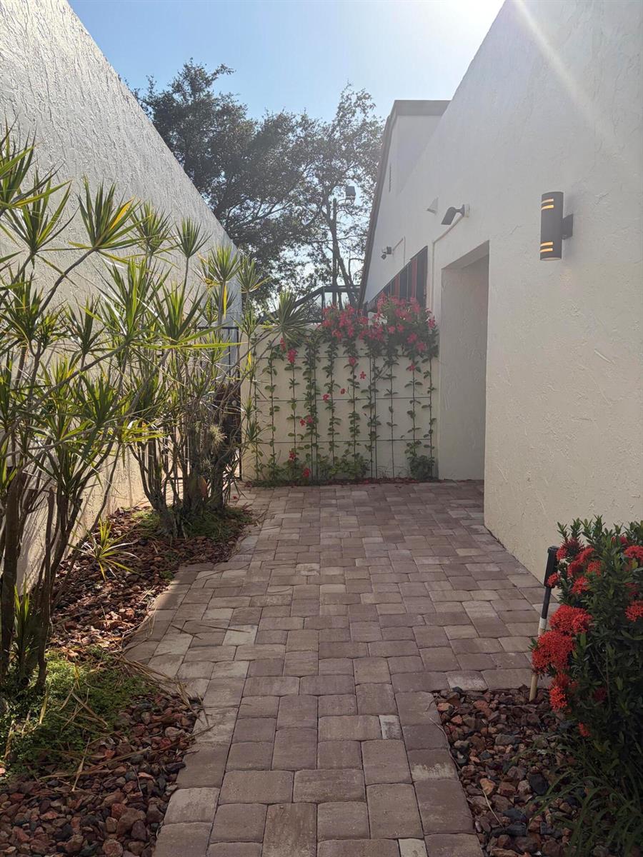 A paved walkway leads between two white walls toward a trellis covered in red flowers — 21435 Campo Allegro Drive, Boca Raton FL 33433, BOCA RATON, FL