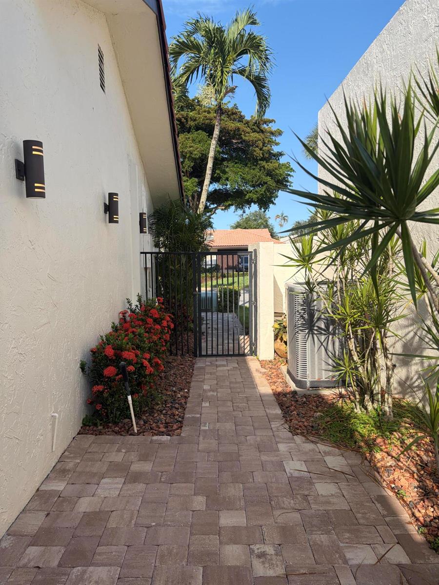 A paved walkway leads between a house wall and a fence toward a metal gate — 21435 Campo Allegro Drive, Boca Raton FL 33433, BOCA RATON, FL