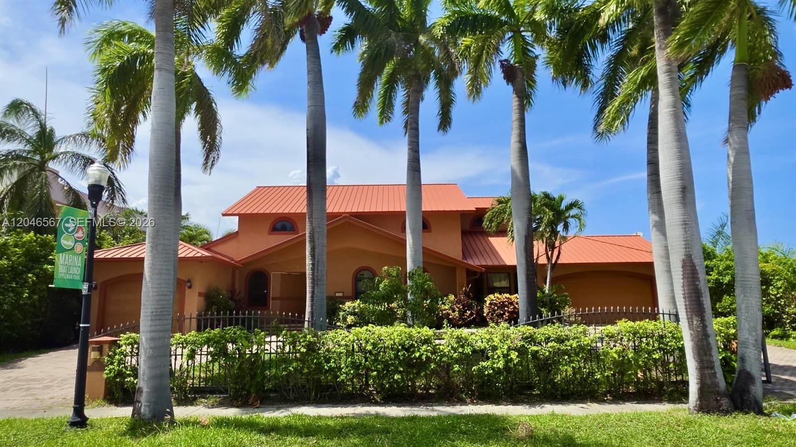 A two-story house with a red metal roof stands behind a hedge and palm trees — 741 Tyler St # 0, Hollywood FL 33019, HOLLYWOOD, FL