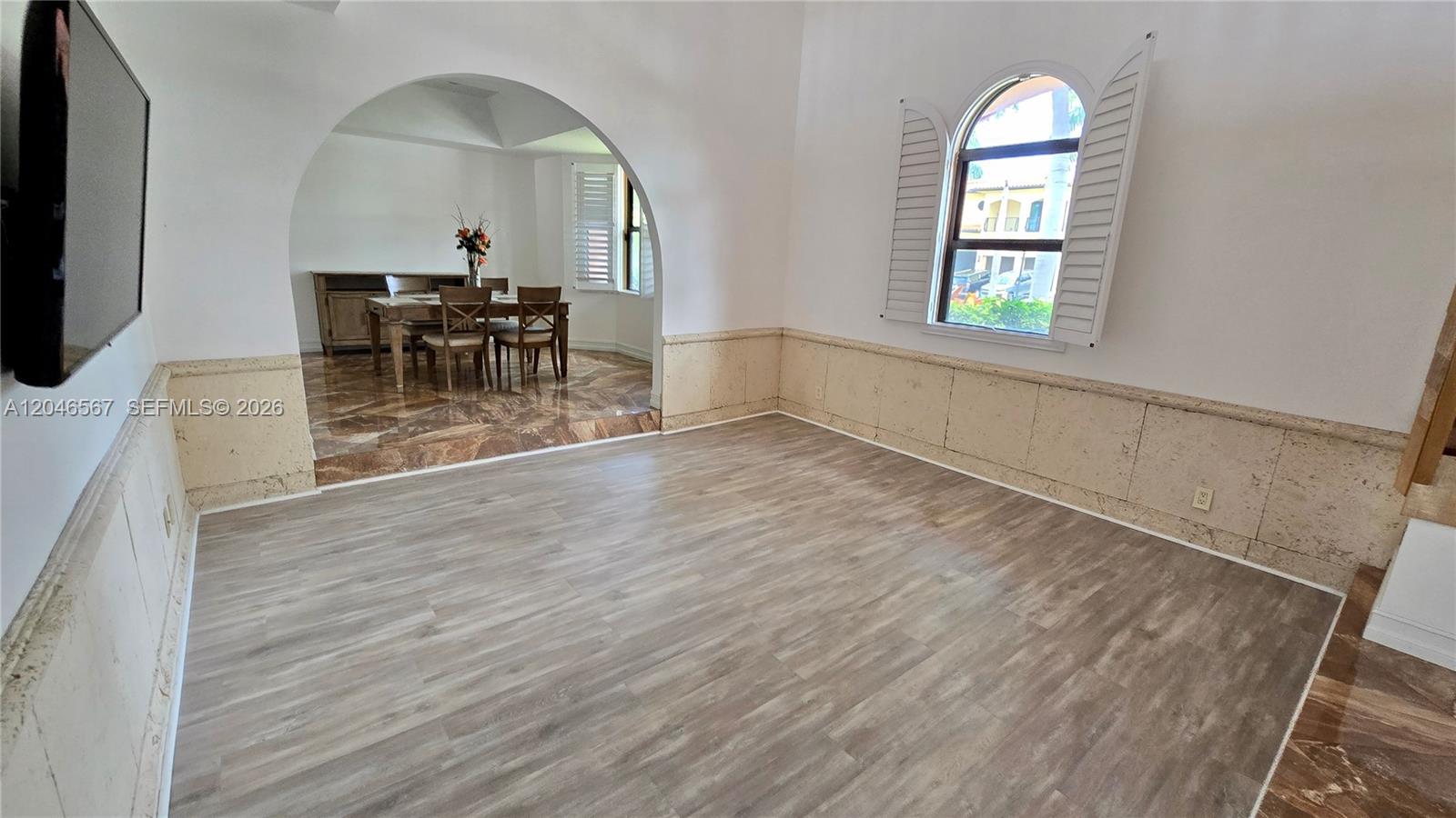 A living room with wood-look flooring and stone wainscoting leads to a raised dining area — 741 Tyler St # 0, Hollywood FL 33019, HOLLYWOOD, FL