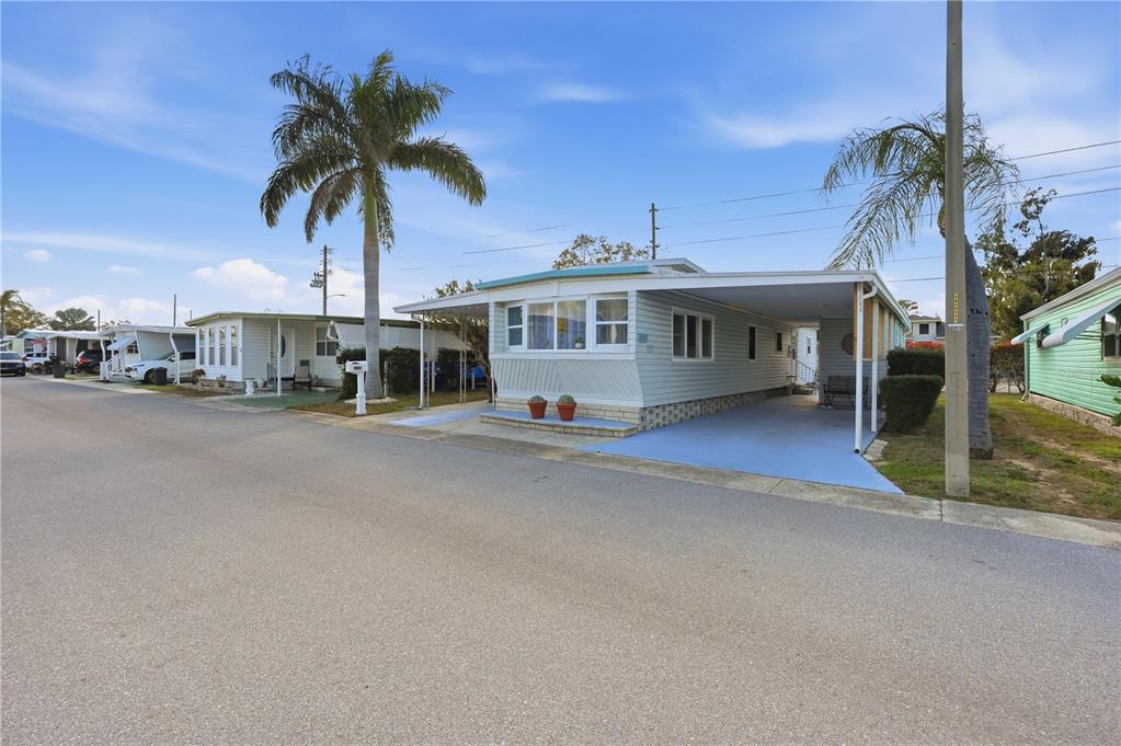 A light-colored mobile home with a carport and palm trees sits along a paved street — 82008 A STREET N UNIT 8, PINELLAS PARK, FL
