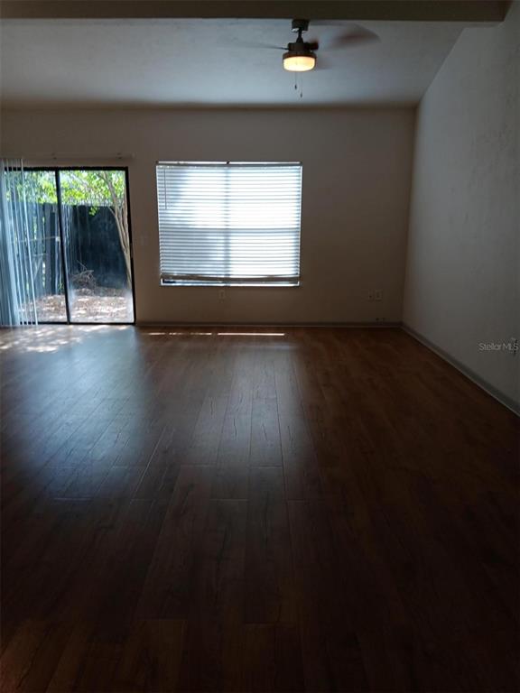 An empty living room features dark wood-look flooring, a ceiling fan, and a sliding glass door — 4419 SW 20TH LANE, GAINESVILLE, FL