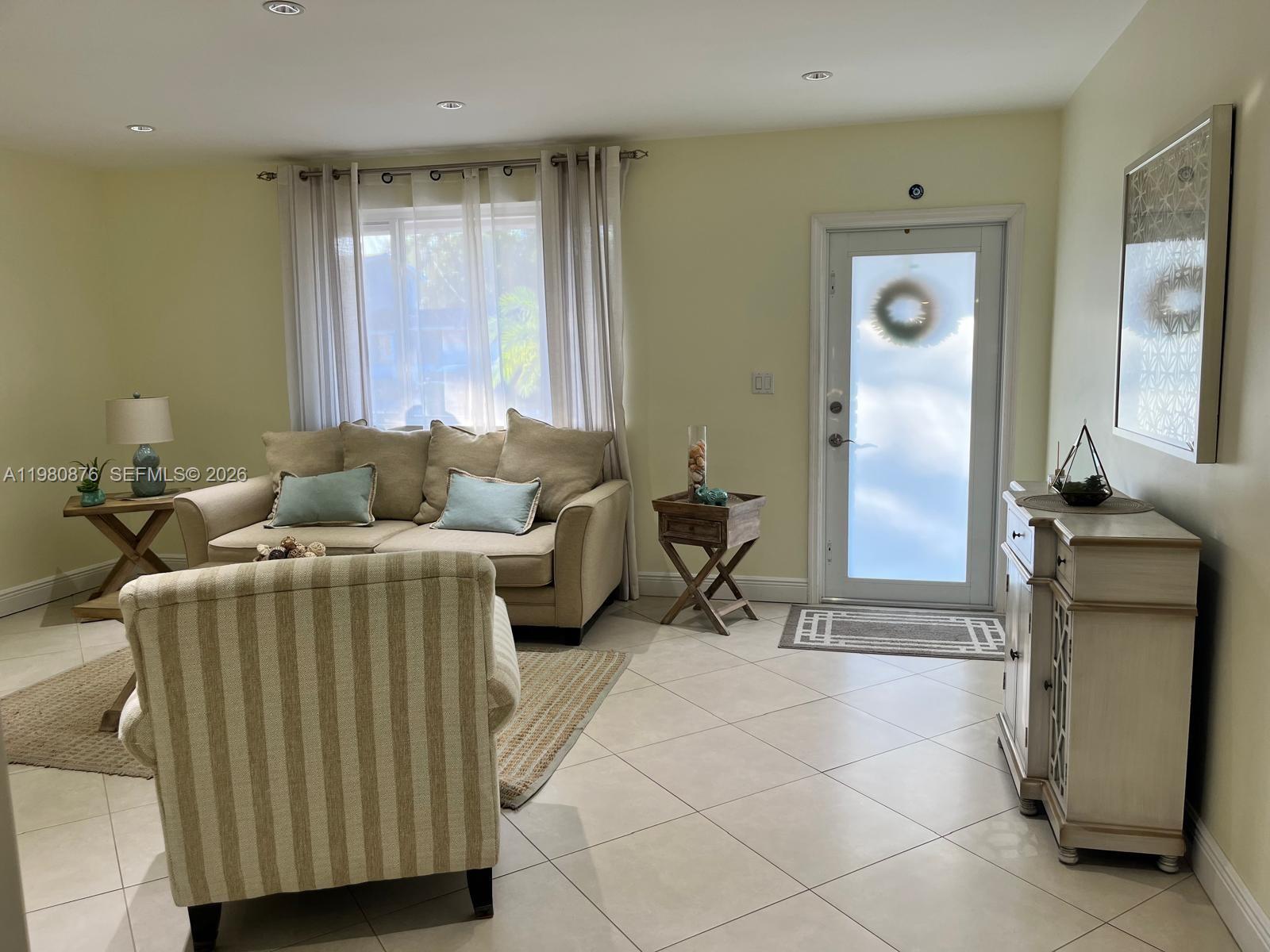 A living room features a beige sofa, striped armchair, tile flooring, and a glass-paneled front door — 685 W 77th St, Hialeah FL 33014, HIALEAH, FL