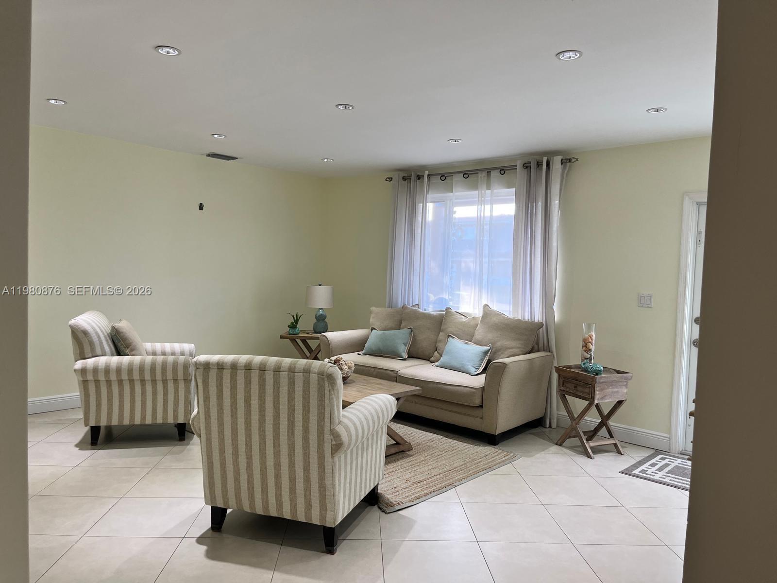 A living room features beige walls, tile flooring, a sofa, and two striped armchairs — 685 W 77th St, Hialeah FL 33014, HIALEAH, FL