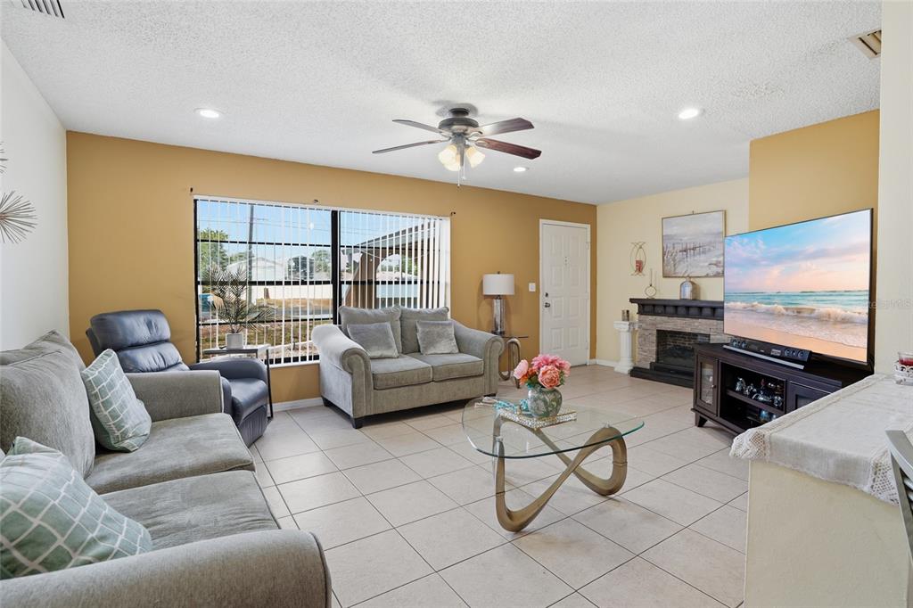 A living room features tile flooring, a fireplace, a ceiling fan, and neutral-toned walls — 10164 GIFFORD DRIVE, SPRING HILL, FL