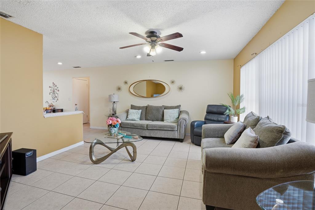 A living room features tile flooring, two gray sofas, a glass coffee table, and ceiling fan — 10164 GIFFORD DRIVE, SPRING HILL, FL