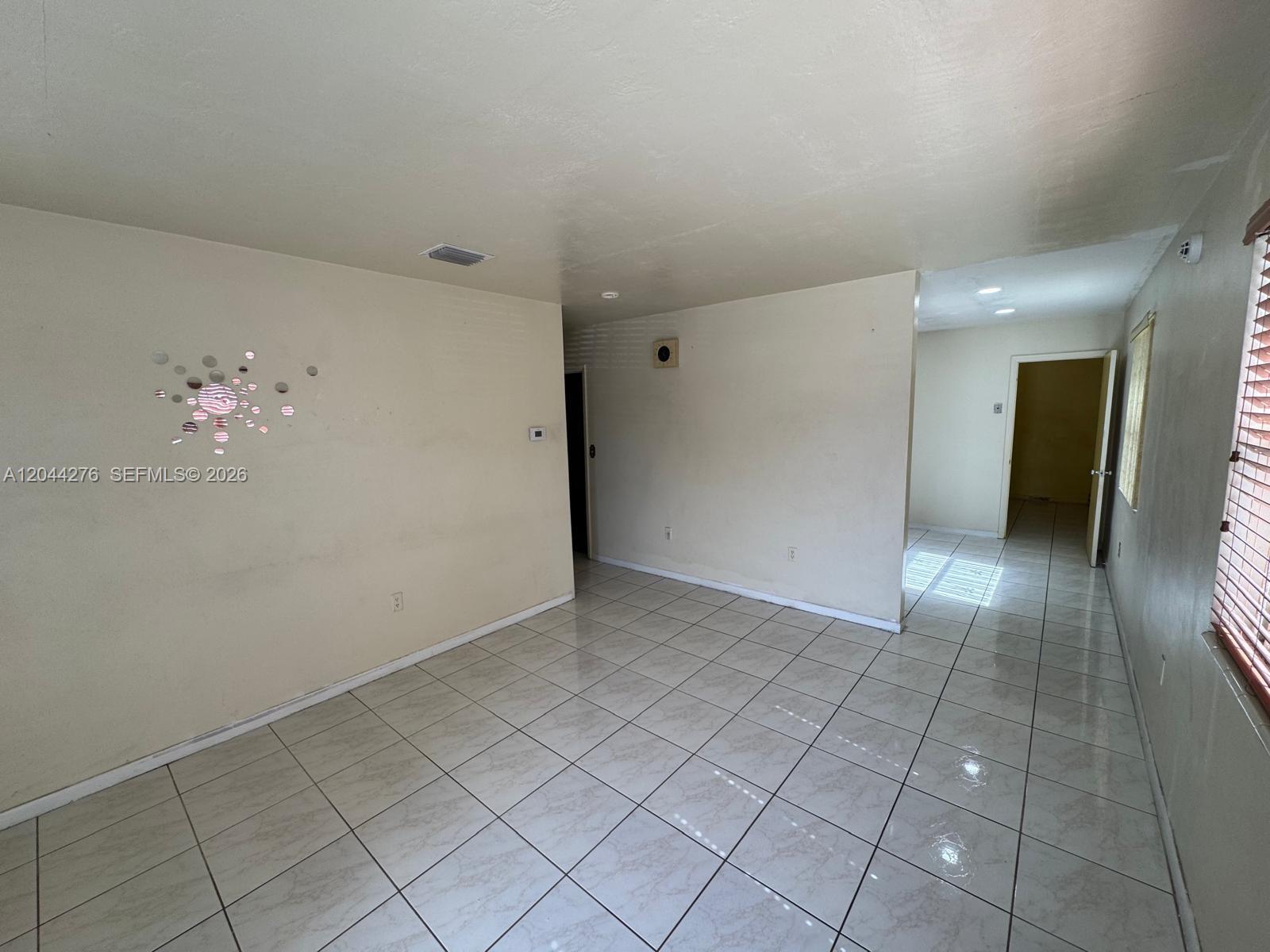 A living room with light-colored tile floors, beige walls, and a decorative wall mirror — 2428 NW 82nd St # 2428, Miami FL 33147, MIAMI, FL