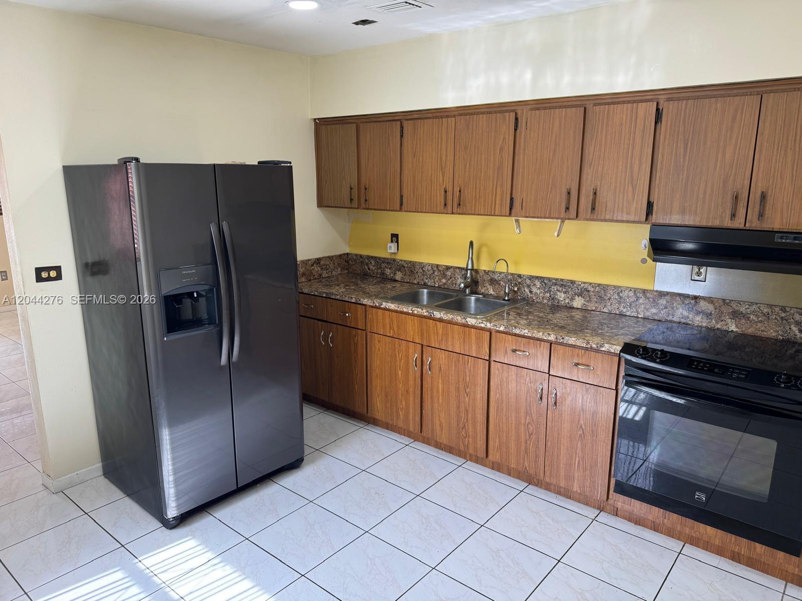 A kitchen features wood cabinets, granite countertops, a stainless steel sink, and black appliances — 2428 NW 82nd St # 2428, Miami FL 33147, MIAMI, FL