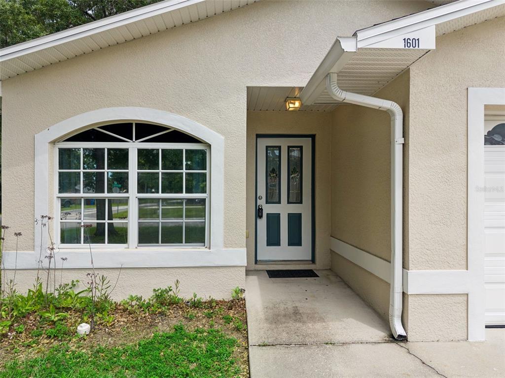 The exterior of a house features a beige stucco facade, a front door, and a window — 1601 WYOMING AVENUE, ST CLOUD, FL