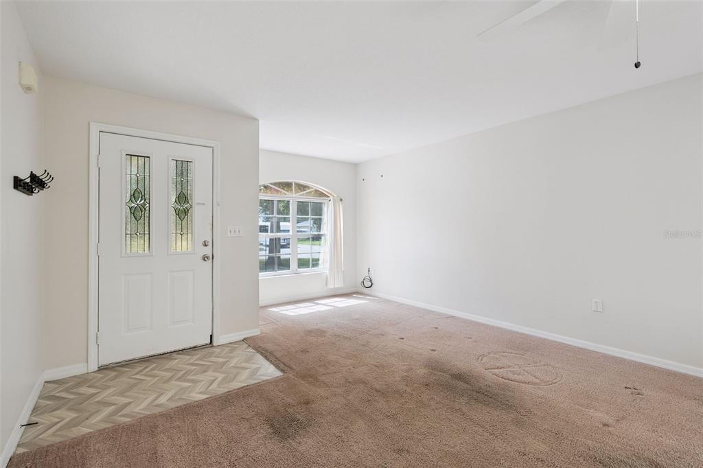 An empty living room features beige carpet, a white front door, and an arched window — 1601 WYOMING AVENUE, ST CLOUD, FL