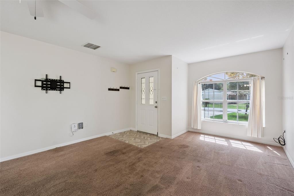 A carpeted living room features a front door, a large arched window, and wall-mounted brackets — 1601 WYOMING AVENUE, ST CLOUD, FL