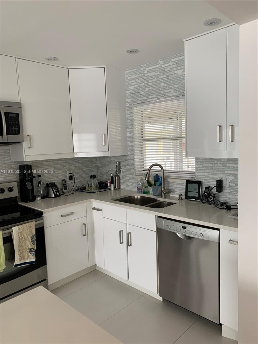 A modern kitchen features white cabinets, stainless steel appliances, and a gray tiled backsplash — 1501 Arthur St # 10, Hollywood FL 33020, HOLLYWOOD, FL