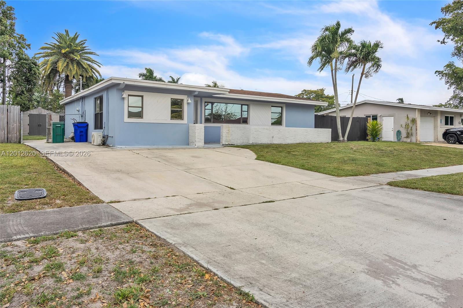 A light blue single-story house features a concrete driveway, white brick accents, and palm trees — 6133 NW 20th St, Margate FL 33063, MARGATE, FL