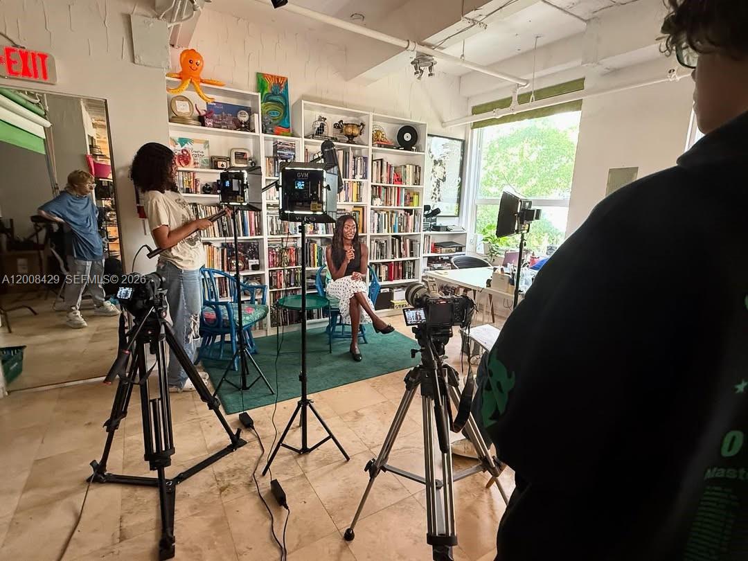 A person is being filmed in a room with floor-to-ceiling bookshelves and large windows — 168 SE 1st St # 400, Miami FL 33131, MIAMI, FL