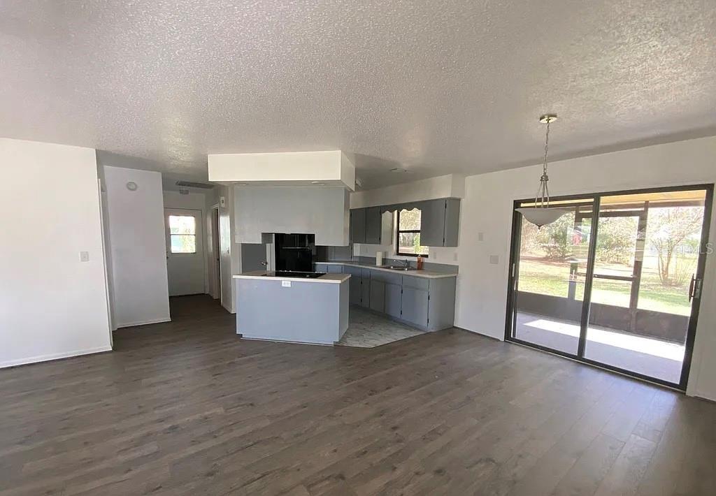 An open-concept kitchen with gray cabinets and a central island overlooks a living area — 35 ABERDEEN CIRCLE, LEESBURG, FL