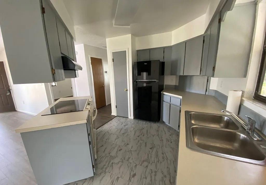 A kitchen features gray cabinets, a black refrigerator, a double sink, and light-colored countertops — 35 ABERDEEN CIRCLE, LEESBURG, FL