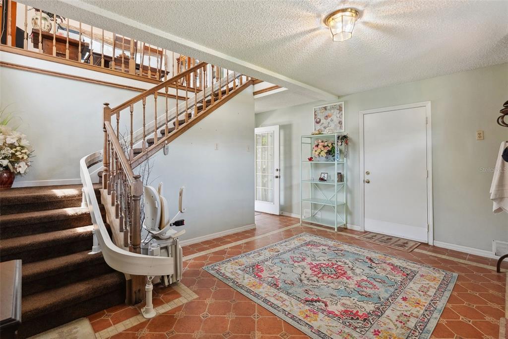 An entryway features a staircase with a chair lift, tile flooring, and a patterned rug — 1842 BAYOU GRANDE BOULEVARD NE, ST PETERSBURG, FL