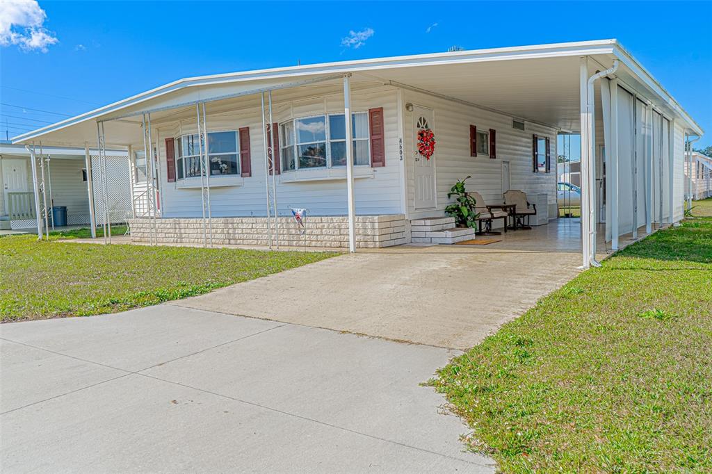A white mobile home features a large carport, a concrete driveway, and a front porch — 4603 NEWCOMB AVENUE, ZEPHYRHILLS, FL