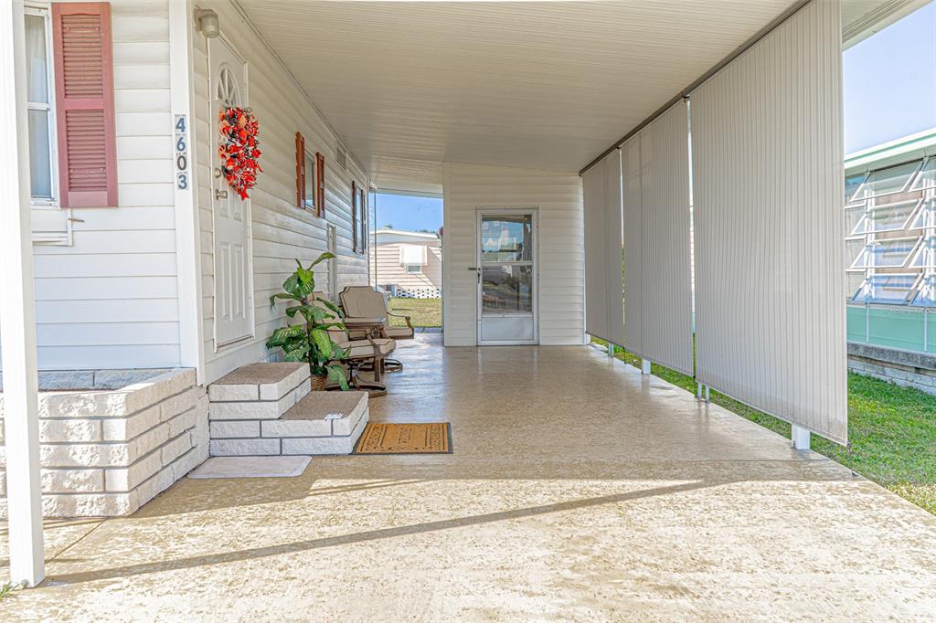 A covered patio features a concrete floor, light siding, and a door with a wreath — 4603 NEWCOMB AVENUE, ZEPHYRHILLS, FL