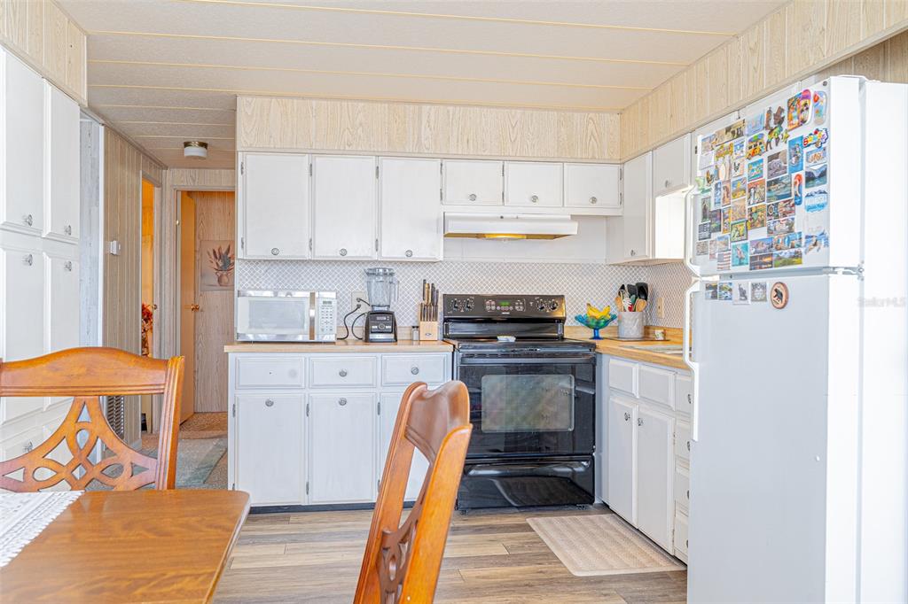 A kitchen features white cabinets, a black stove, a microwave, and a white refrigerator — 4603 NEWCOMB AVENUE, ZEPHYRHILLS, FL