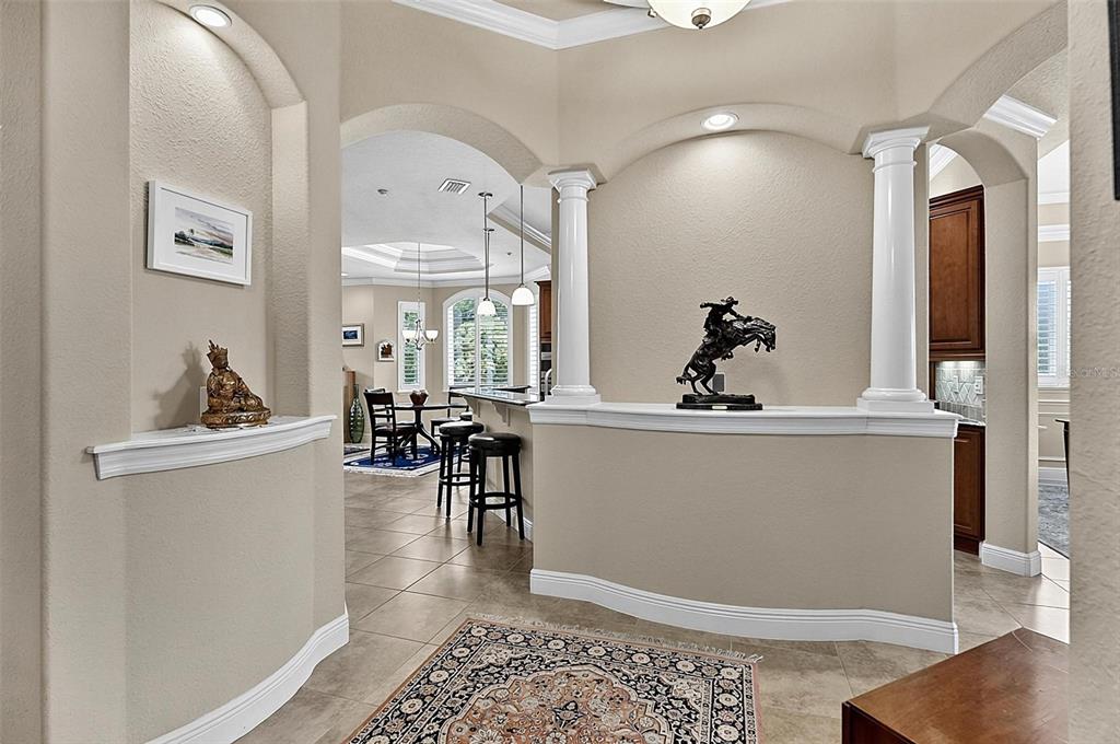 A foyer with arched niches, white columns, and a view into a kitchen and dining area — 200 CEDAR COVE UNIT 205, PALM COAST, FL