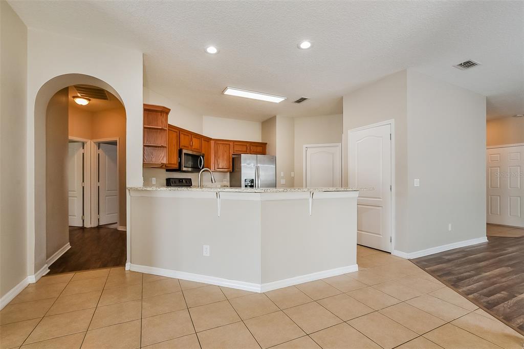 A kitchen with wooden cabinets, granite countertops, and a breakfast bar overlooks a tiled area — 1221 LONGVILLE CIRCLE, TAVARES, FL