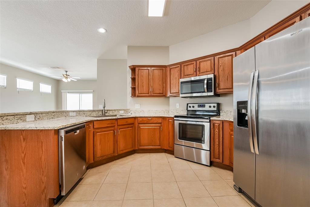 A kitchen with wood cabinets, granite countertops, stainless steel appliances, and beige tile flooring — 1221 LONGVILLE CIRCLE, TAVARES, FL