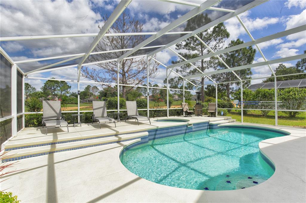 A screened-in pool area features a kidney-shaped pool, a hot tub, and lounge chairs — 1942 BERMUDA POINTE DRIVE, HAINES CITY, FL
