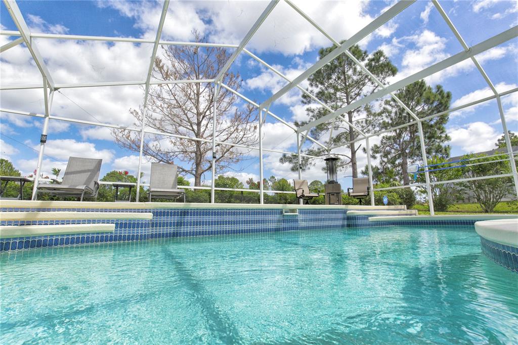 A swimming pool with blue tile trim is enclosed by a white metal screen structure — 1942 BERMUDA POINTE DRIVE, HAINES CITY, FL