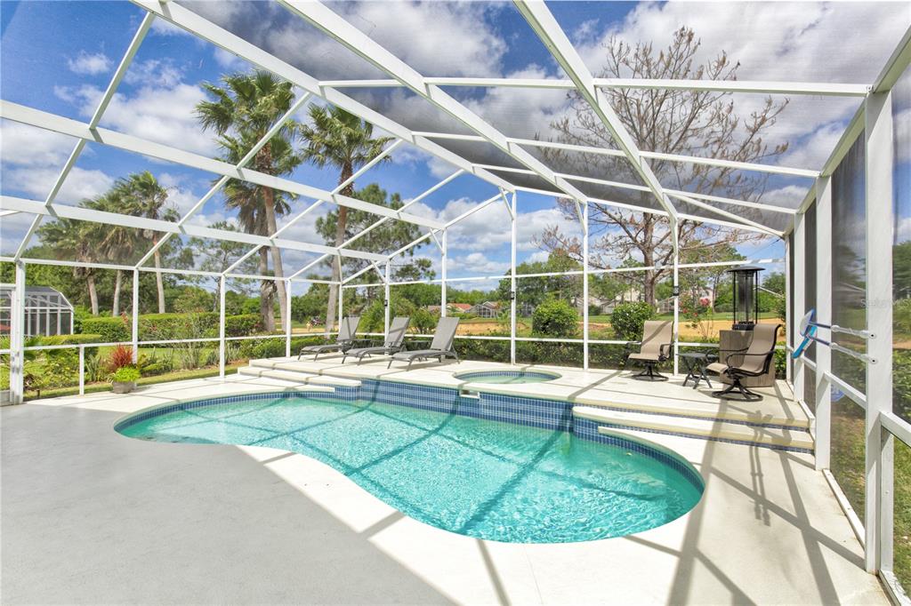 A screened-in pool and spa area with lounge chairs overlooking a grassy landscape — 1942 BERMUDA POINTE DRIVE, HAINES CITY, FL
