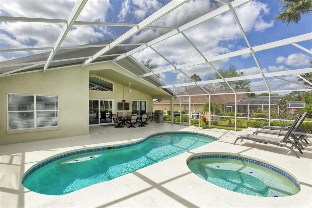 A screened-in patio features a swimming pool, a hot tub, and outdoor dining furniture — 1942 BERMUDA POINTE DRIVE, HAINES CITY, FL