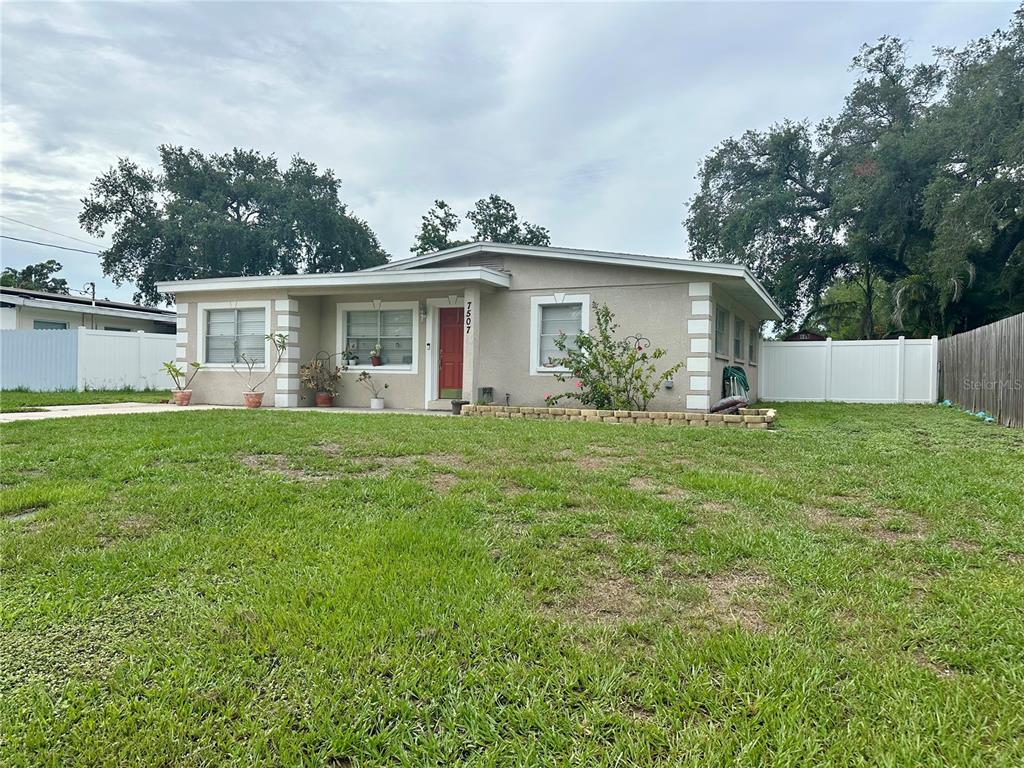 A single-story house with a red front door, light-colored stucco, and a grassy front yard — 7507 CORAL VINE LANE, TAMPA, FL