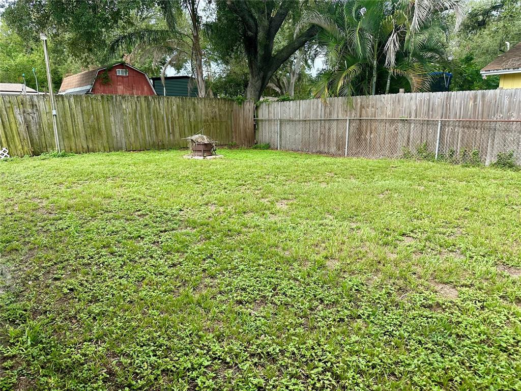 A grassy backyard features a fire pit, a wooden fence, and mature trees — 7507 CORAL VINE LANE, TAMPA, FL