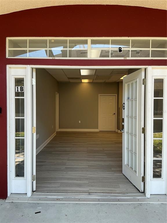An open doorway reveals a vacant commercial office space with light wood-look flooring — 11701 ORPINGTON STREET UNIT 1B, ORLANDO, FL