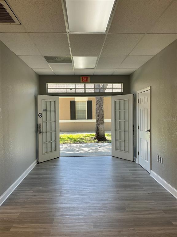 An interior room features light wood-look flooring, a drop ceiling, and open double glass doors — 11701 ORPINGTON STREET UNIT 1B, ORLANDO, FL