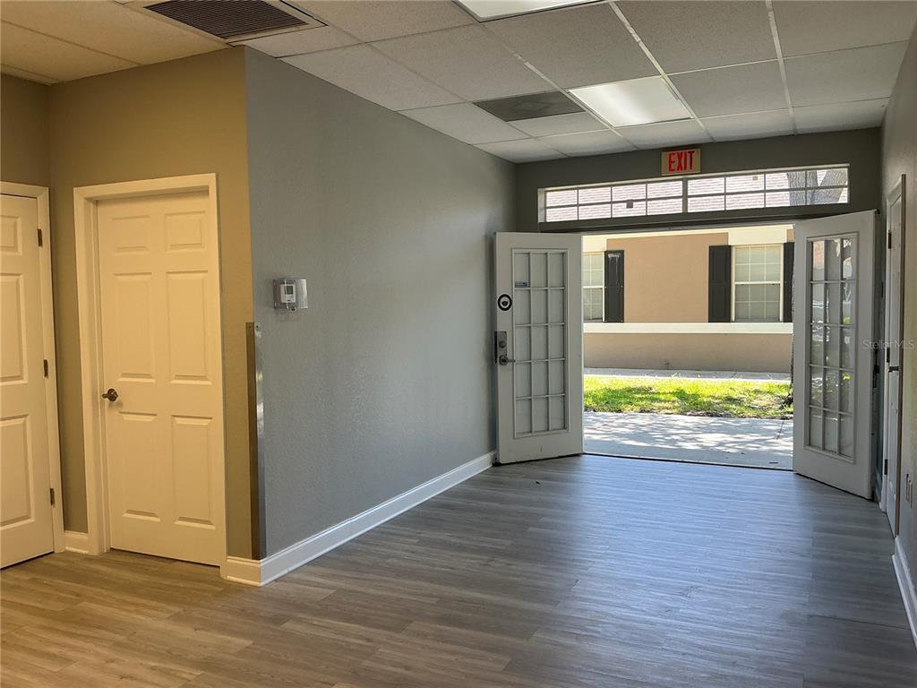 An interior room with light wood-look flooring, gray walls, and double doors opening outdoors — 11701 ORPINGTON STREET UNIT 1B, ORLANDO, FL
