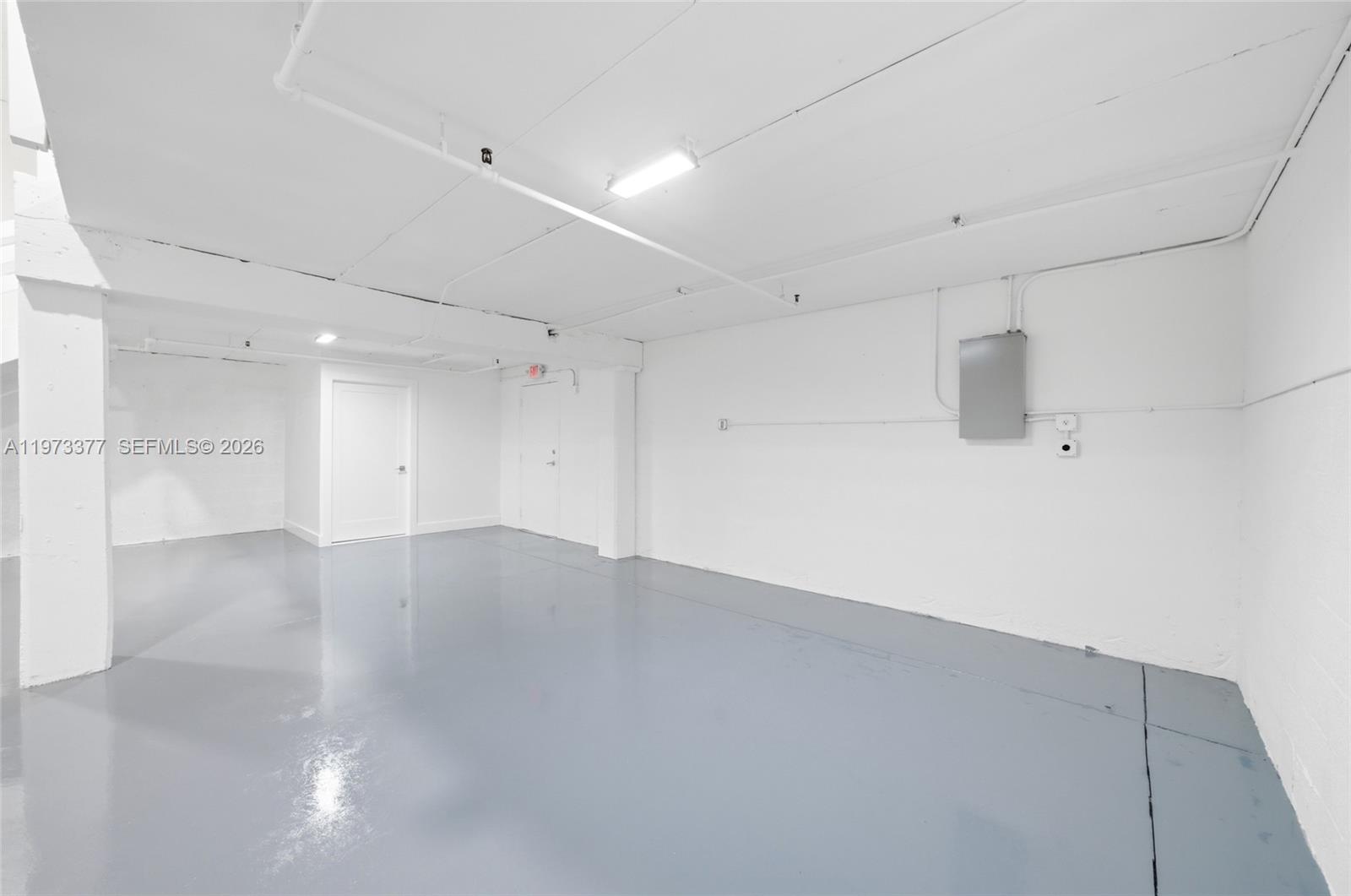 A minimalist, white-walled room features a glossy gray floor and exposed ceiling pipes — 16300 SW 137th Ave # 119, Miami FL 33177, MIAMI, FL