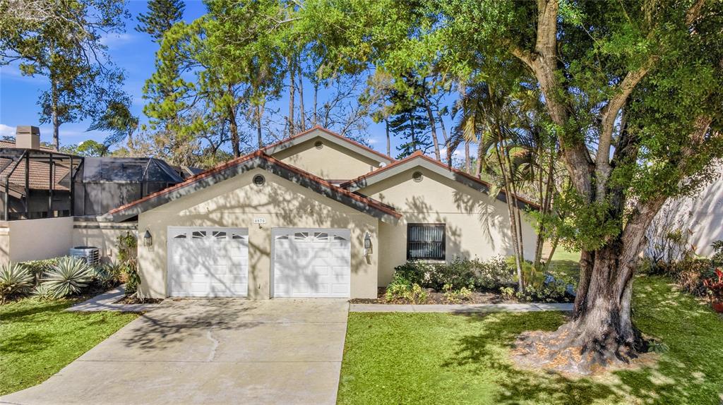 A single-story house with a two-car garage, beige stucco exterior, and a large front tree — 4870 TIVOLI COURT, SARASOTA, FL