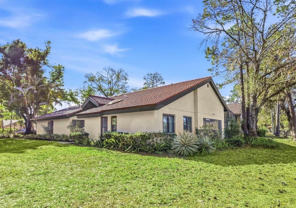A side view of a beige stucco house with a tiled roof and surrounding landscaping — 4870 TIVOLI COURT, SARASOTA, FL