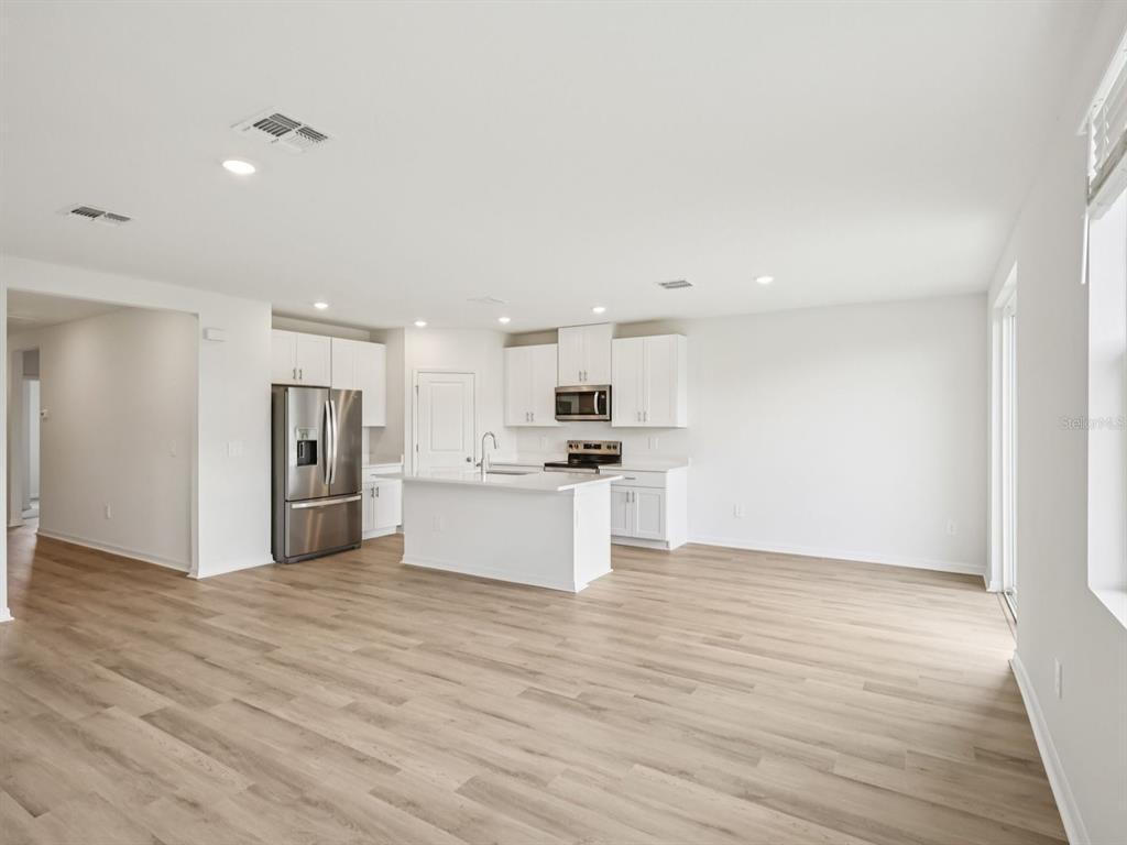 A modern kitchen with white cabinets, stainless steel appliances, and an island overlooks an open-concept living area — 1777 FOREST RUN LANE, AUBURNDALE, FL