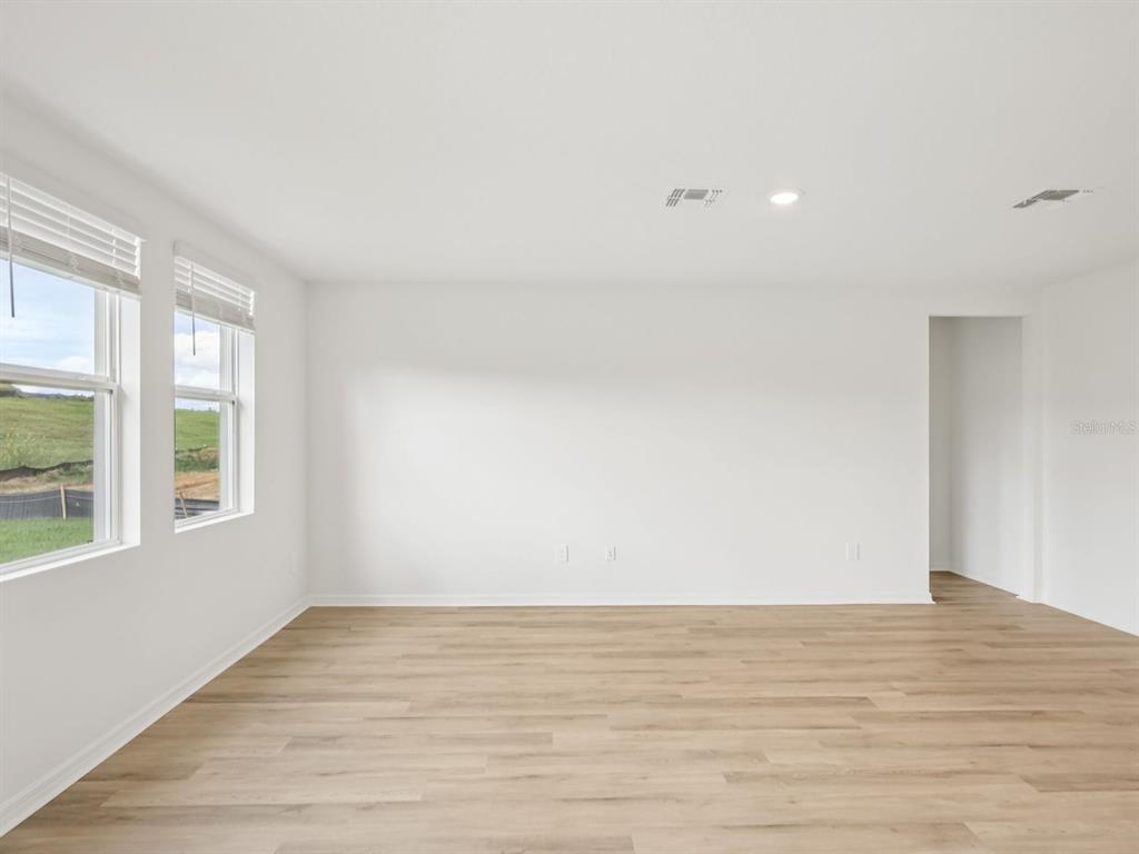 An empty room with white walls, light wood-look flooring, and two windows overlooking a field — 1777 FOREST RUN LANE, AUBURNDALE, FL