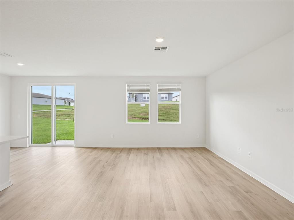 An empty living room features light wood-look flooring, white walls, and a sliding glass door — 1777 FOREST RUN LANE, AUBURNDALE, FL