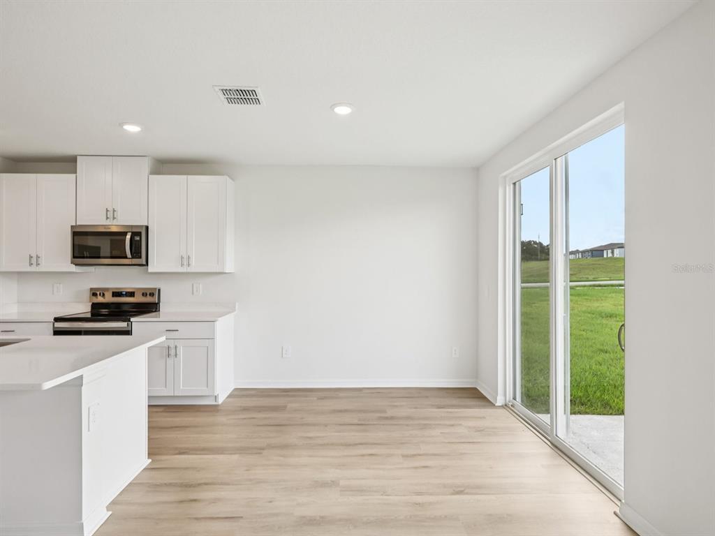 A kitchen with white cabinets and light wood flooring opens to a patio through sliding doors — 1777 FOREST RUN LANE, AUBURNDALE, FL