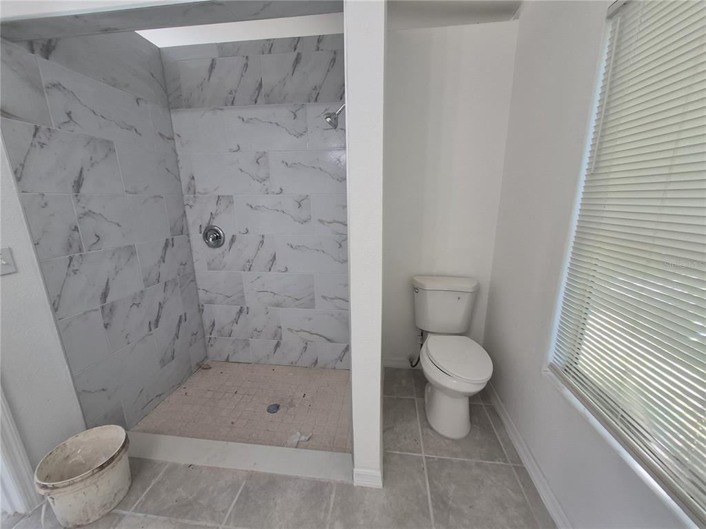A bathroom features a walk-in shower with marble-look tile and a white toilet — 6500 SE 25TH AVENUE, OCALA, FL