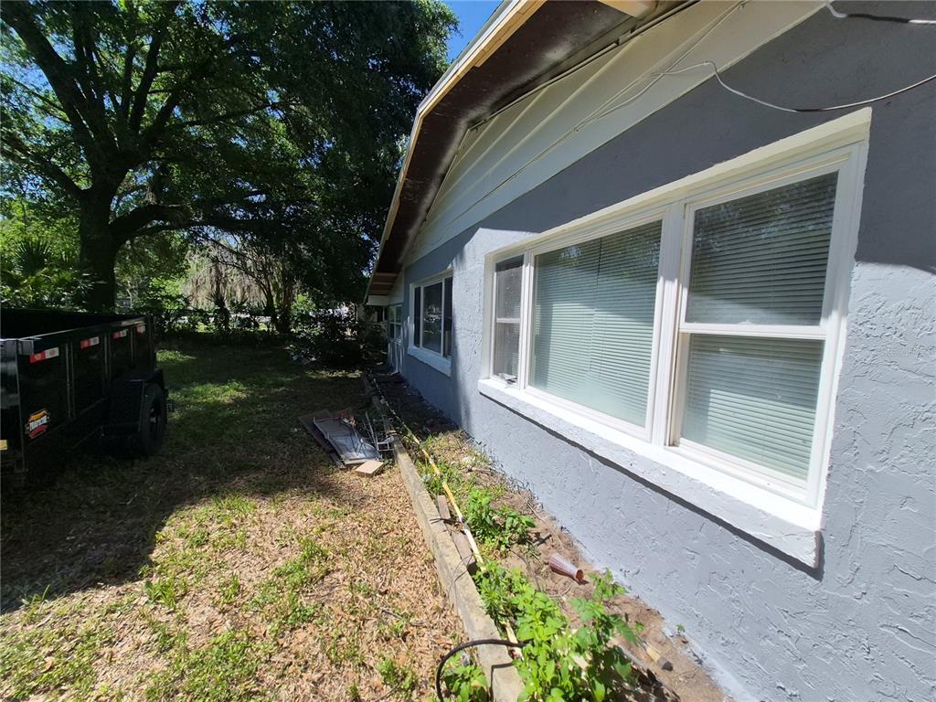 The exterior side of a gray house features white-framed windows and a small garden bed — 6500 SE 25TH AVENUE, OCALA, FL