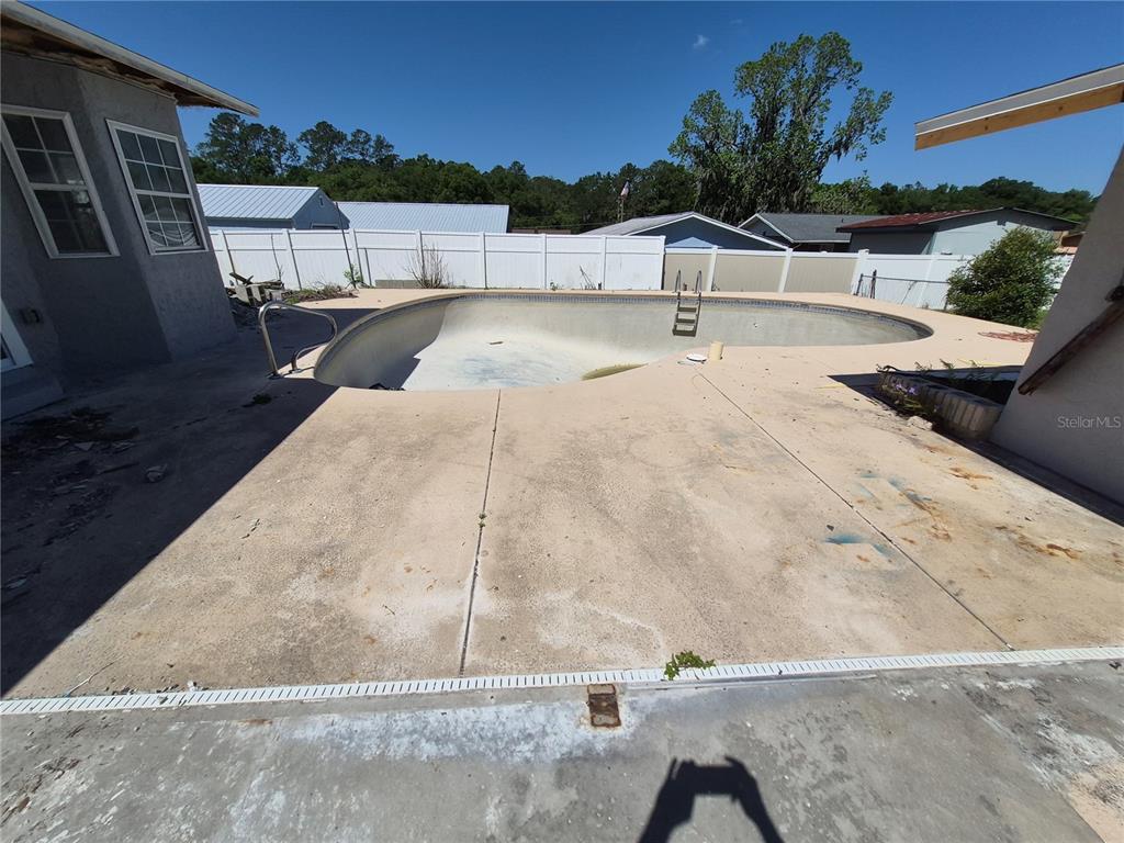 An empty, kidney-shaped swimming pool sits in a backyard with a concrete patio — 6500 SE 25TH AVENUE, OCALA, FL