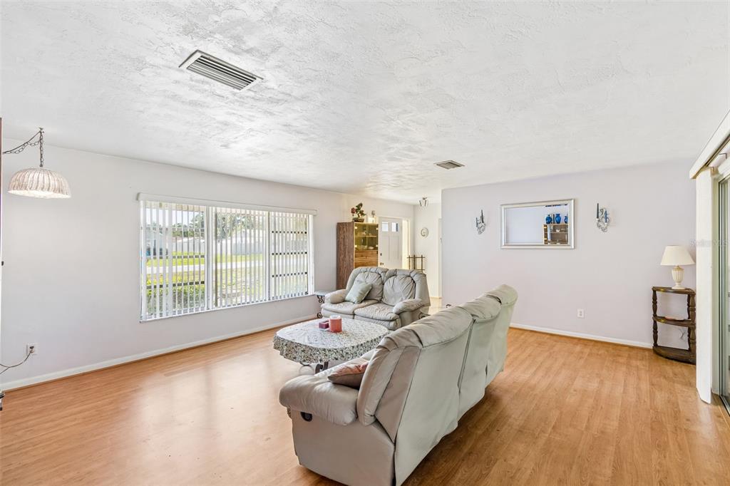 A living room features light wood-look flooring, a textured ceiling, and two light-colored sofas — 2059 WATERFALL DRIVE, SPRING HILL, FL